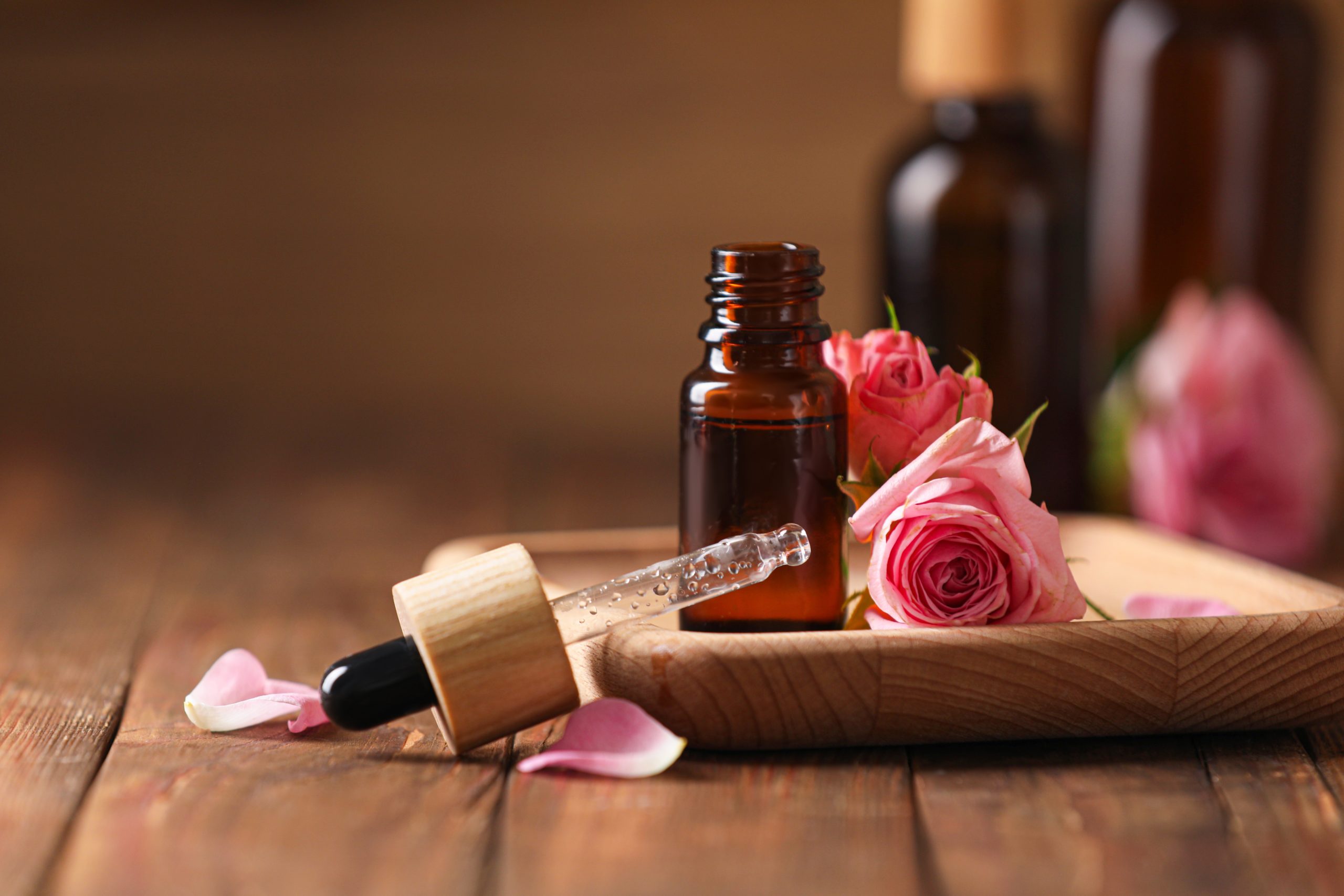 Bottle,Of,Essential,Rose,Oil,And,Flowers,On,Wooden,Table,